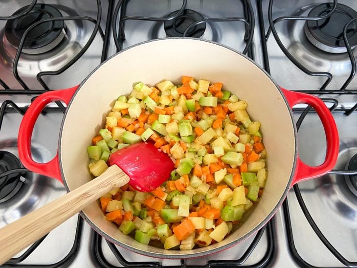 Uma panela contendo cebola, alho, chuchu, cenoura e batata refogados.