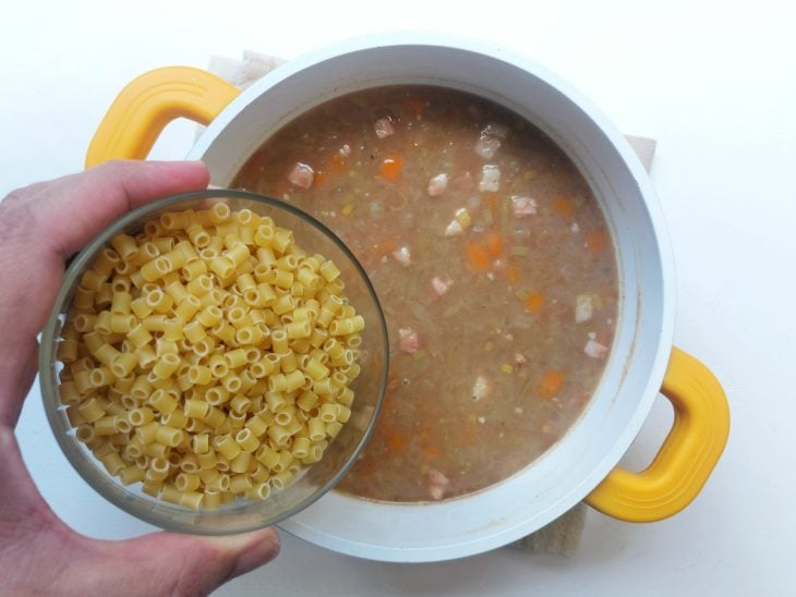 Macarrão sendo adicionado na panela com sopa de feijão.