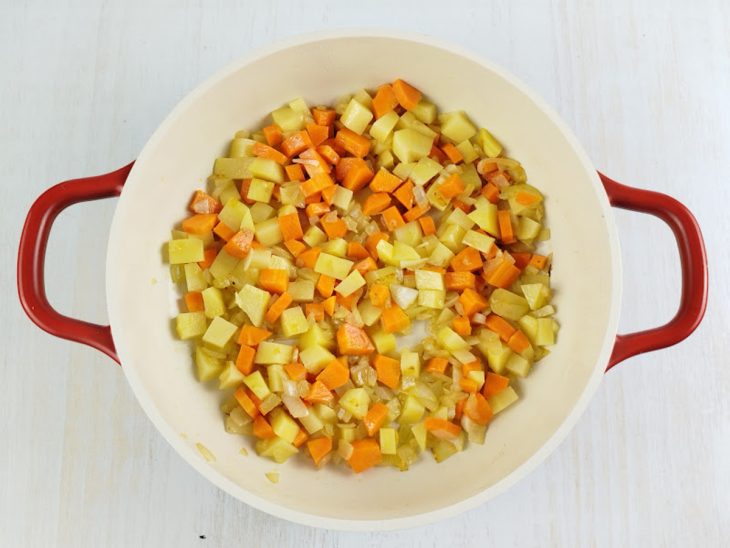 Cenoura e batata sendo adicionadas à panela e misturadas com a cebola.