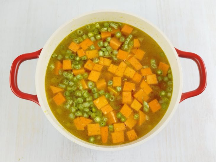 Abóbora e vagem picadas entrando na panela após a fervura.