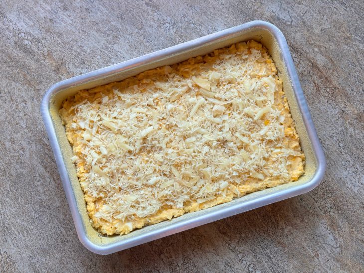 massa de sopa paraguaia despejada no tabuleiro e finalizada com queijo ralado.