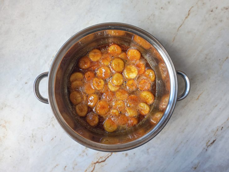 Na panela, bananas picadas adicionadas e misturadas a calda.