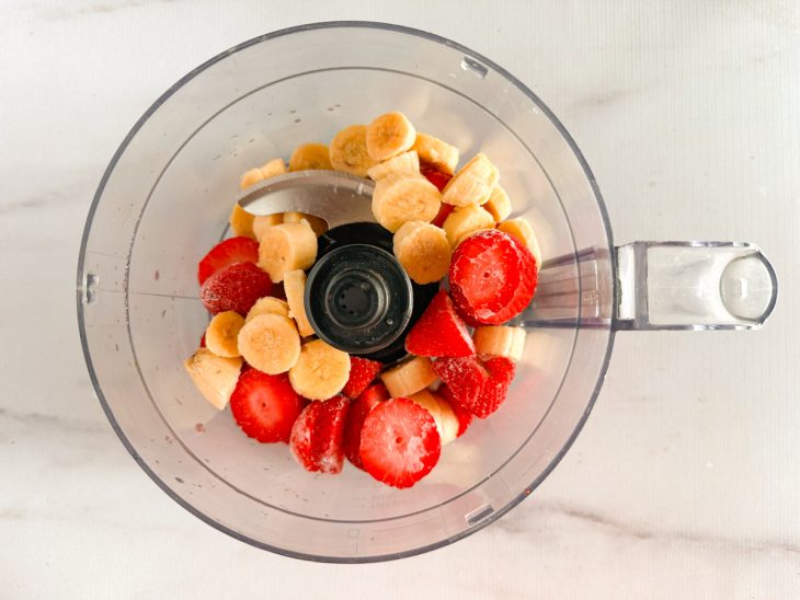 No copo do processador, as frutas congeladas dispostas.