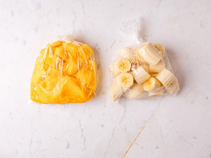 Bananas e mangas picadas dentro de saquinhos plásticos sobre uma bancada.