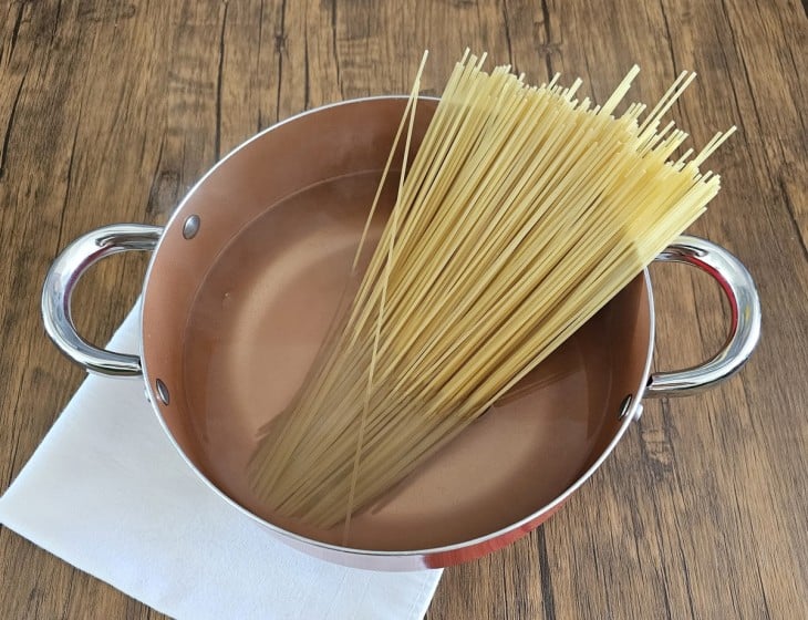 Panela com água e macarrão longo e fino.