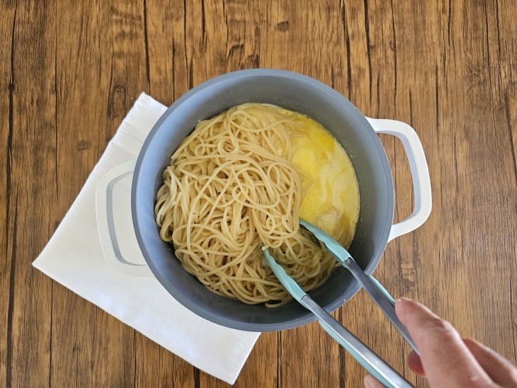 Massa de spaghetti sendo misturada ao molho na panela.