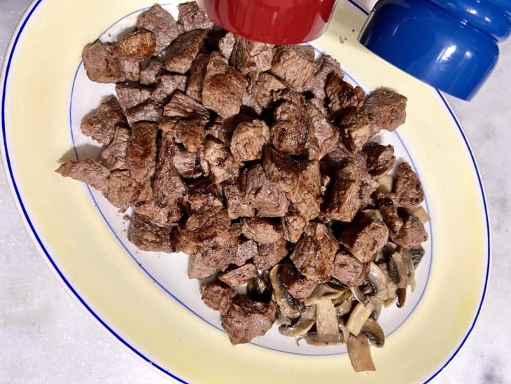 Um prato com carne sendo temperada.