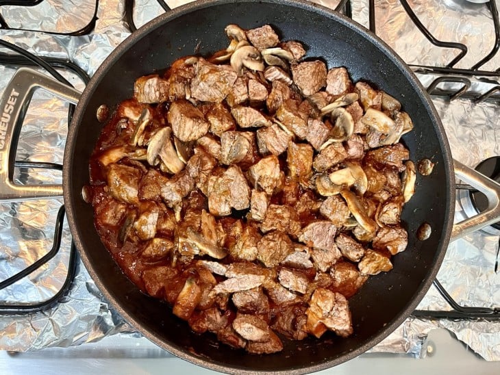 Uma frigideira com molho, cogumelos e carne.