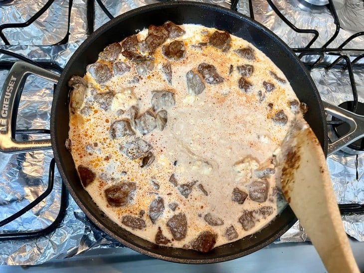 Uma frigideira com molho, cogumelos, carne e creme de leite.