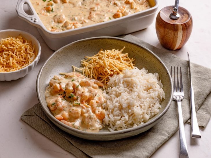 Prato com arroz, strogonoff de camarão e batata palha sobre uma bancada.