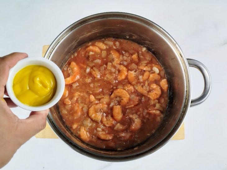 Molho de tomate e mostarda adicionados e incorporados na panela com camarão.