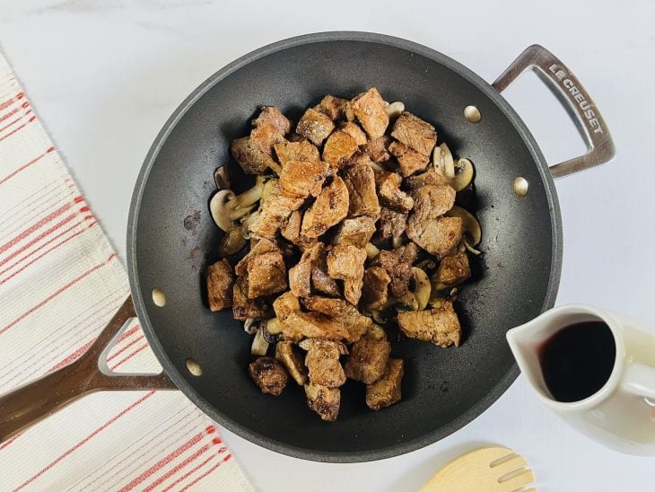 Uma panela com carne, cogumelos, cebola, alho e vinho ao fogo.