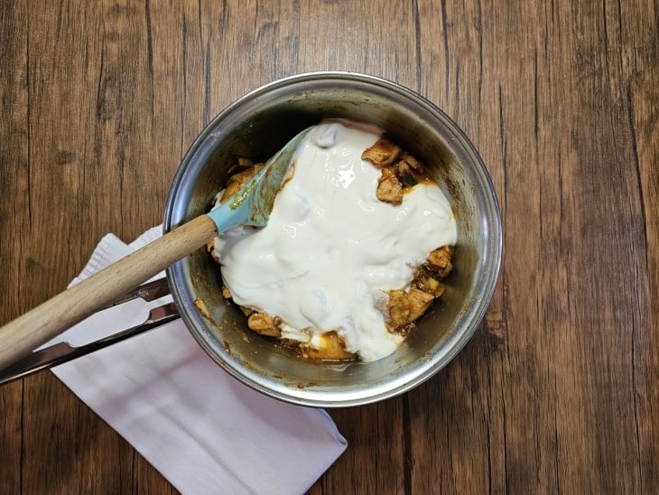 Uma panela contendo cubos de frango, cogumelos fatiados e creme de leite.