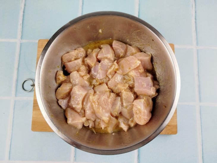 Cubos de frango temperados em um recipiente.