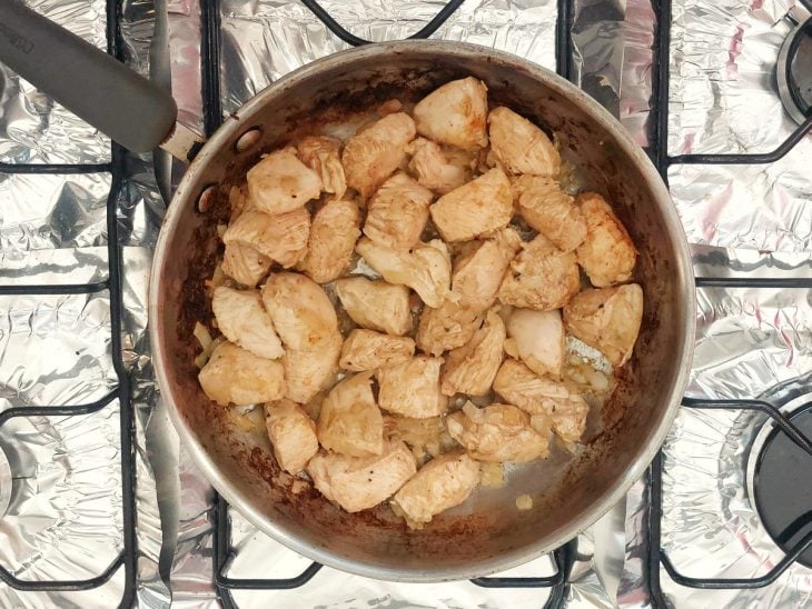 Uma panela com frango refogado e temperos.