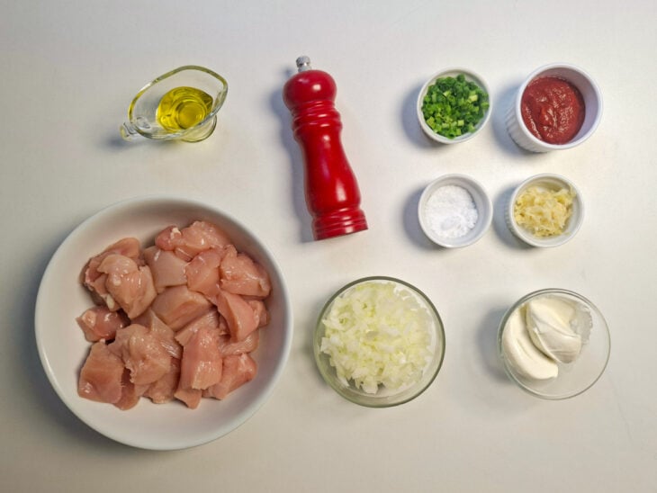 Ingredientes dispostos na bancada com cubos de frango, alho amassado, cebola picada, molho de tomate, creme de ricota e ervas.