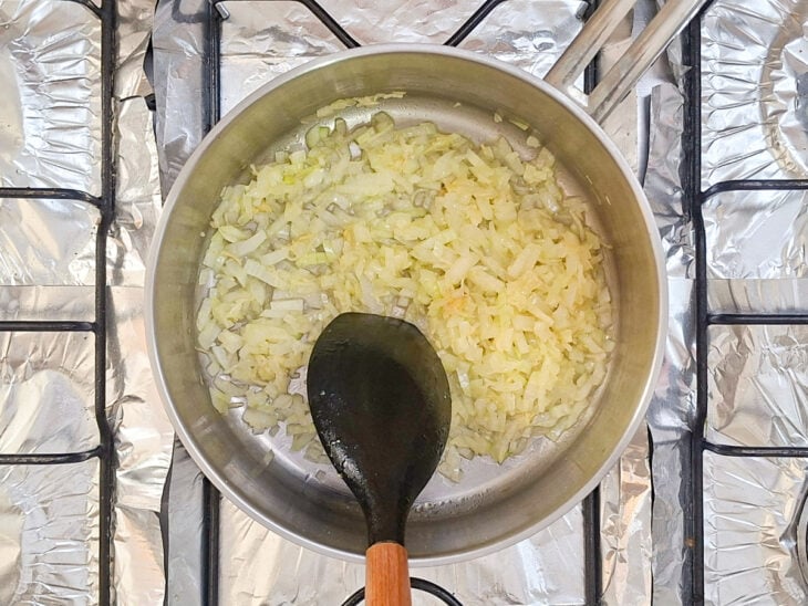 Cebola em cubinhos adicionada ao alho sendo refogada na panela até ficar translúcida.