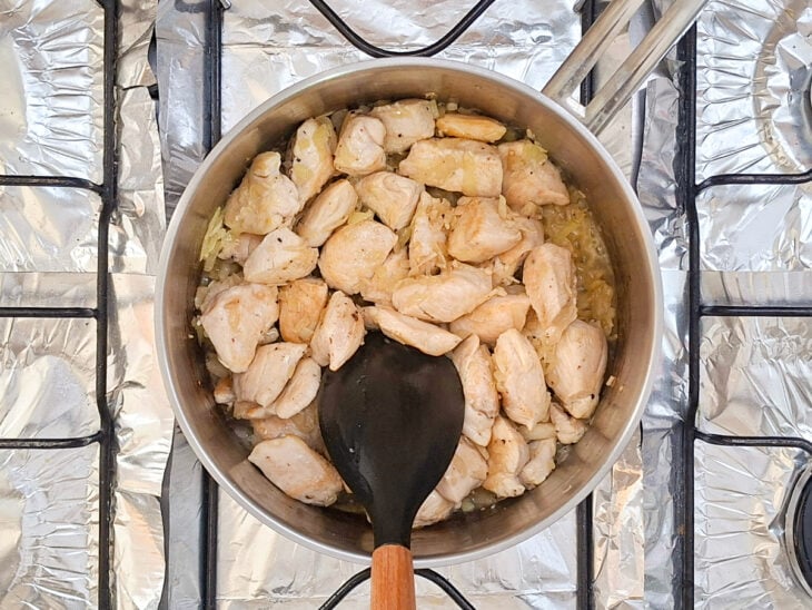 Cubos médios de peito de frango sendo fritos e selados no refogado de cebola e alho.