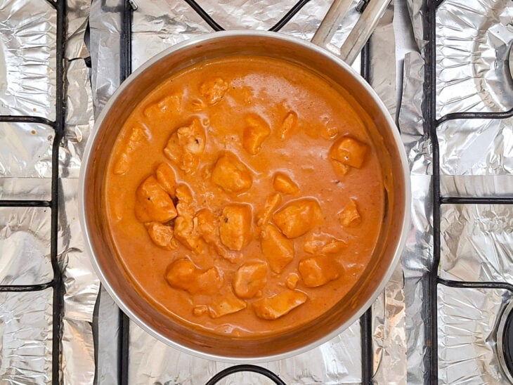 Mistura líquida de ricota sendo despejada sobre o frango ao molho de tomate na panela.
