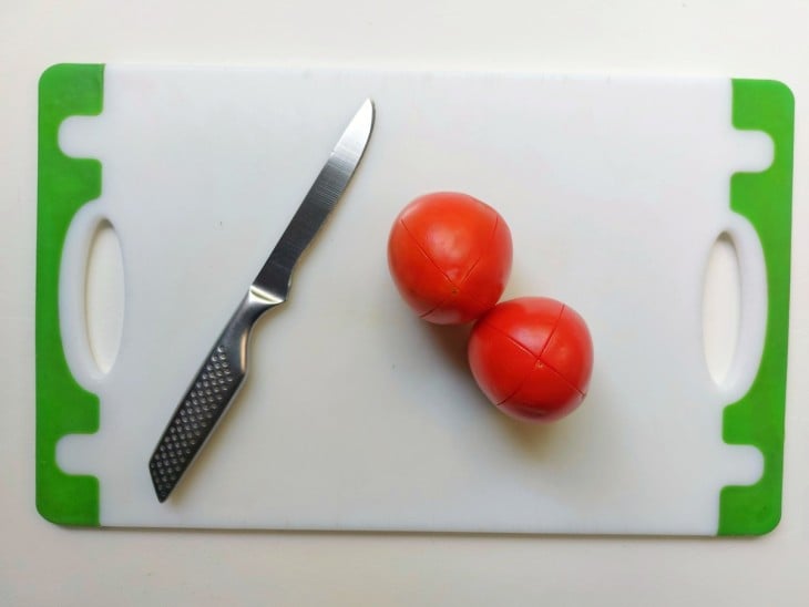 2 tomates cortados superficialmente em cima de uma tábua.