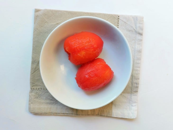 2 tomates sem pele em um recipiente.