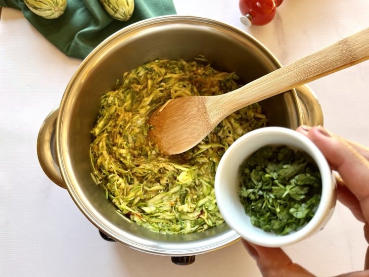 Uma panela com abobrinha refogada ralada e cheiro-verde.