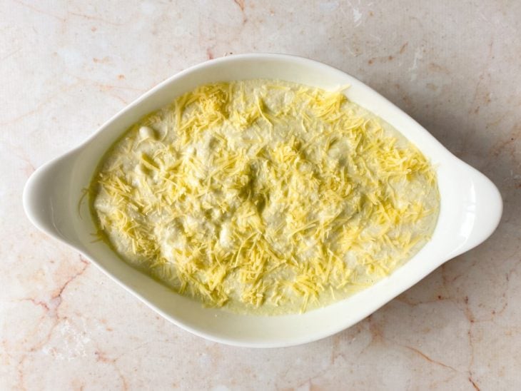 Mistura acomodada em um recipiente untado e enfarinhado, e parmesão salpicado na superfície.