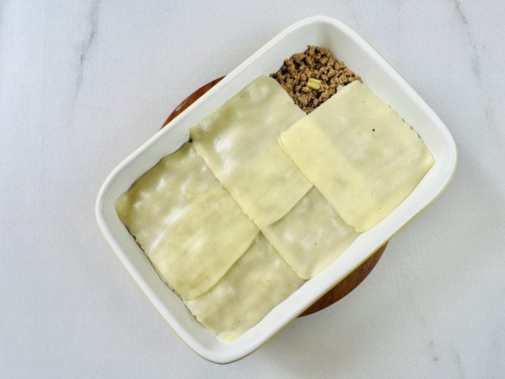 Refratário com uma camada da massa, recheio de carne moída e fatias de mussarela.