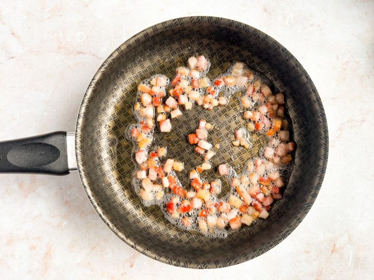 Bacon cortado em cubinhos sendo dourado na frigideira.