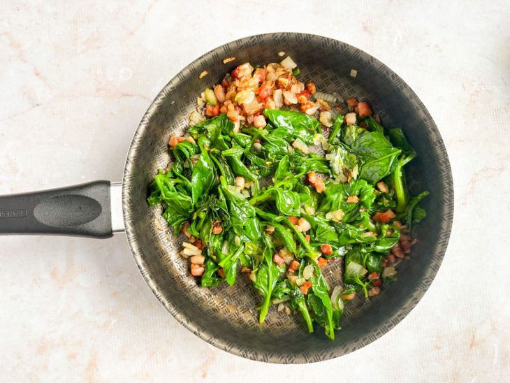 Espinafre sendo adicionado ao refogado, murchando na panela.