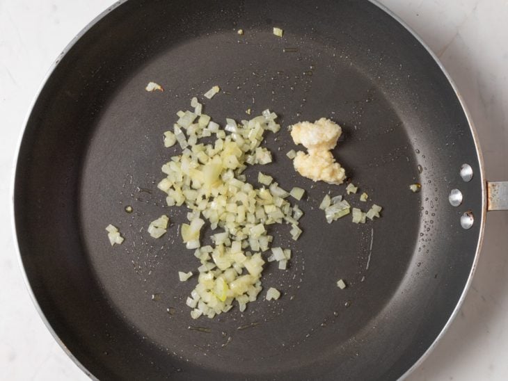 Alho e cebola picados na frigideira a dourar.