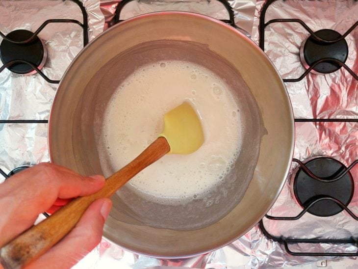 Uma tigela com a mistura de suspiro acima de uma panela com água ao fogo.