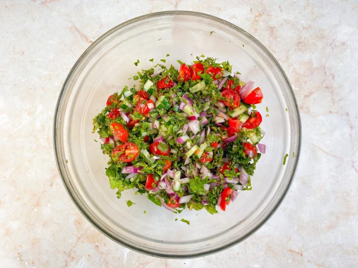 Recipiente de vidro com salsinha, hortelã, tomate, cebola e pepino misturados.