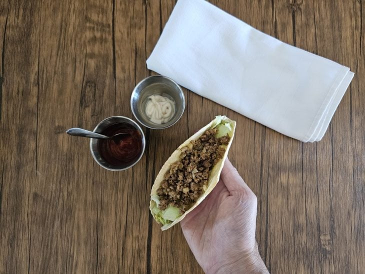 Um taco sendo recheado com guacamole, alface, carne e molhos.