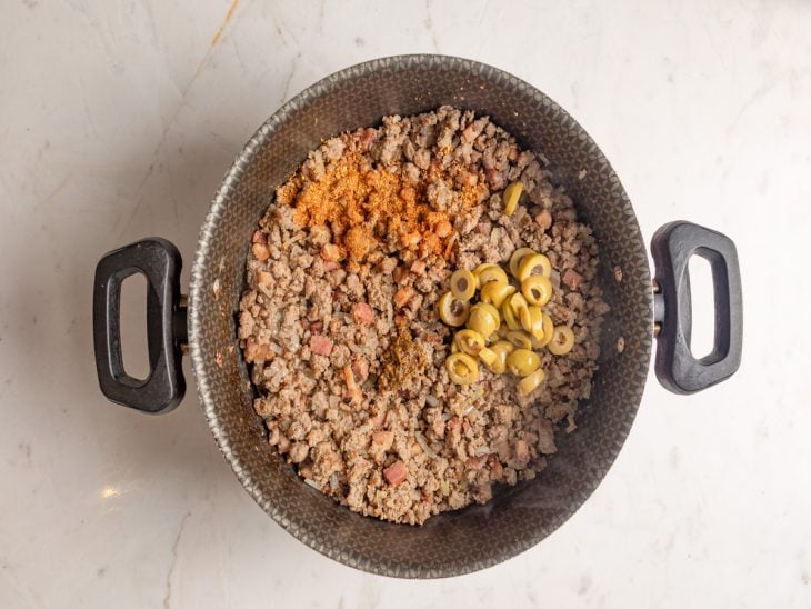 Panela com bacon, carne moída, alho, cebola, azeitonas e temperos.