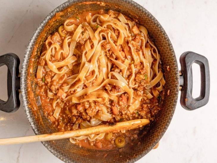 Uma panela com macarrão e molho misturados.