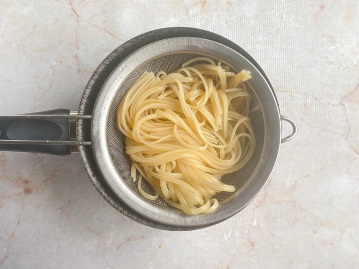 Macarrão cozido e escorrido em uma peneira sobre uma panela.