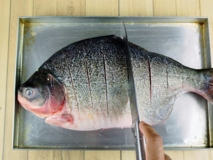 Peixe em uma forma com cortes feitos por uma faca.