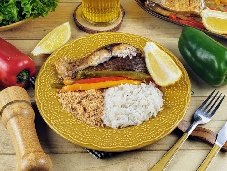 Peixe servido com arroz, pimentões e farofa em um prato individual amarelo.