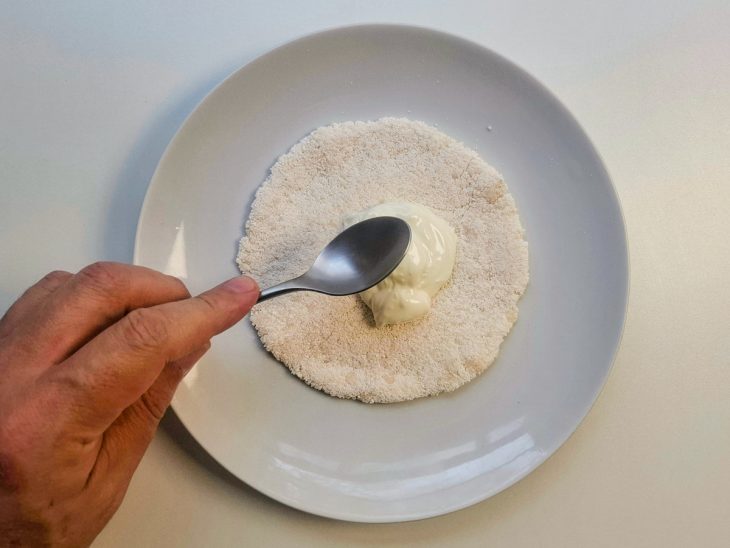 Na tapioca reservada, uma colher de requeijão sendo espalhada.