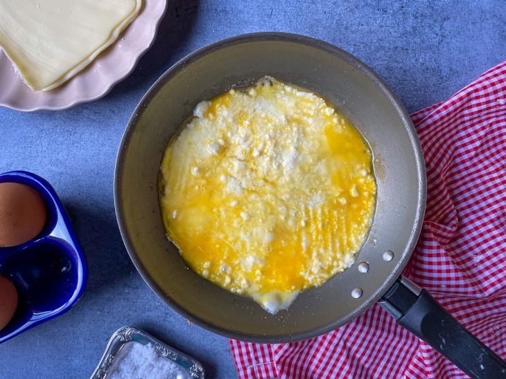Uma frigideira com ovo, fatias de queijo e tapioca.