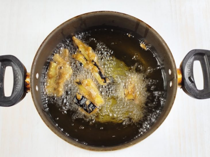 Berinjelas fritando em óleo numa panela.