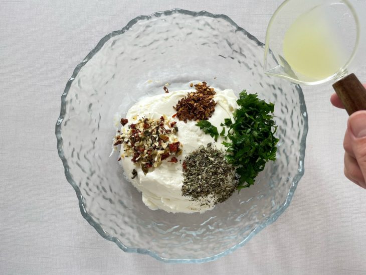 Cream cheese sendo misturado com ervas, especiarias e suco de limão em uma tigela.