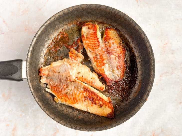 Filés de tilápia sendo temperados com alho, ervas e sal em um recipiente.