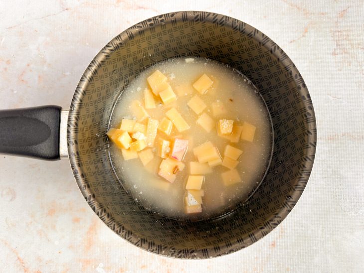 Queijos e caldo dissolvido sendo aquecidos em panela para formar o molho.