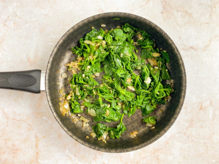 Na frigideira, estão reunidos o alho e o espinafre.