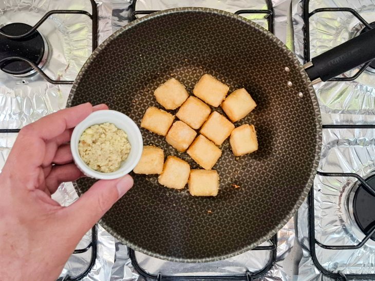 Na frigideira, alho e gengibre sendo adicionados ao tofu.