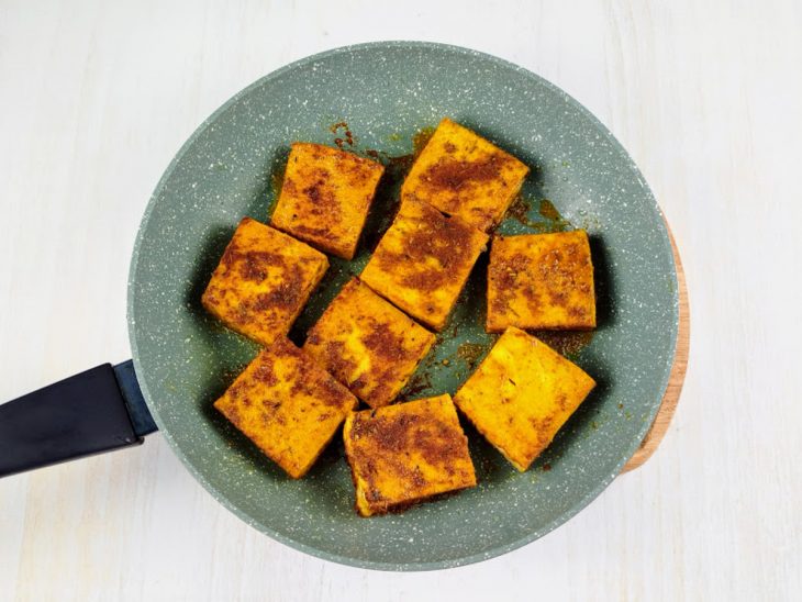 Pedaços de tofu grelhando na frigideira com azeite.