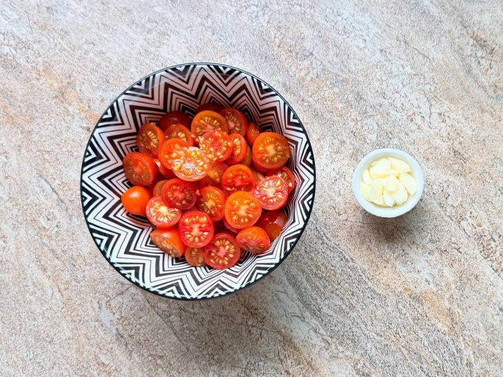 Tomates cereja cortados ao meio e alho fatiado.