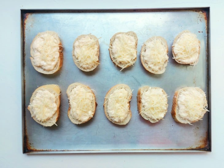 Queijo salpicado por cima das fatias de pão com maionese.